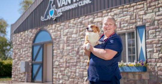 Glenda Henle Van Wyk ’02 and Lilly the Corgi posing outside Van Wyk Veterinary Clinic in Pella.